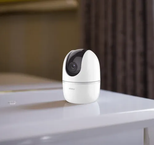 IMOU Ranger 2 indoor pan-and-tilt camera in white, standing on a table with a curtain behind it
